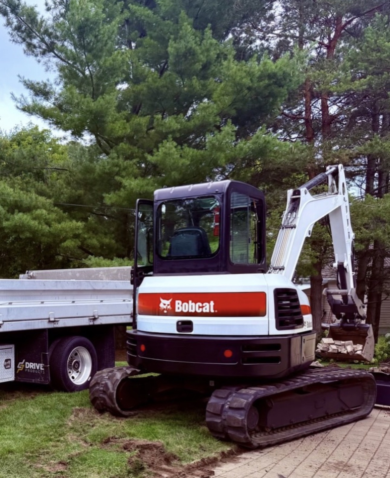Bobcat E55 excavator parked beside a float trailer on a residential property
